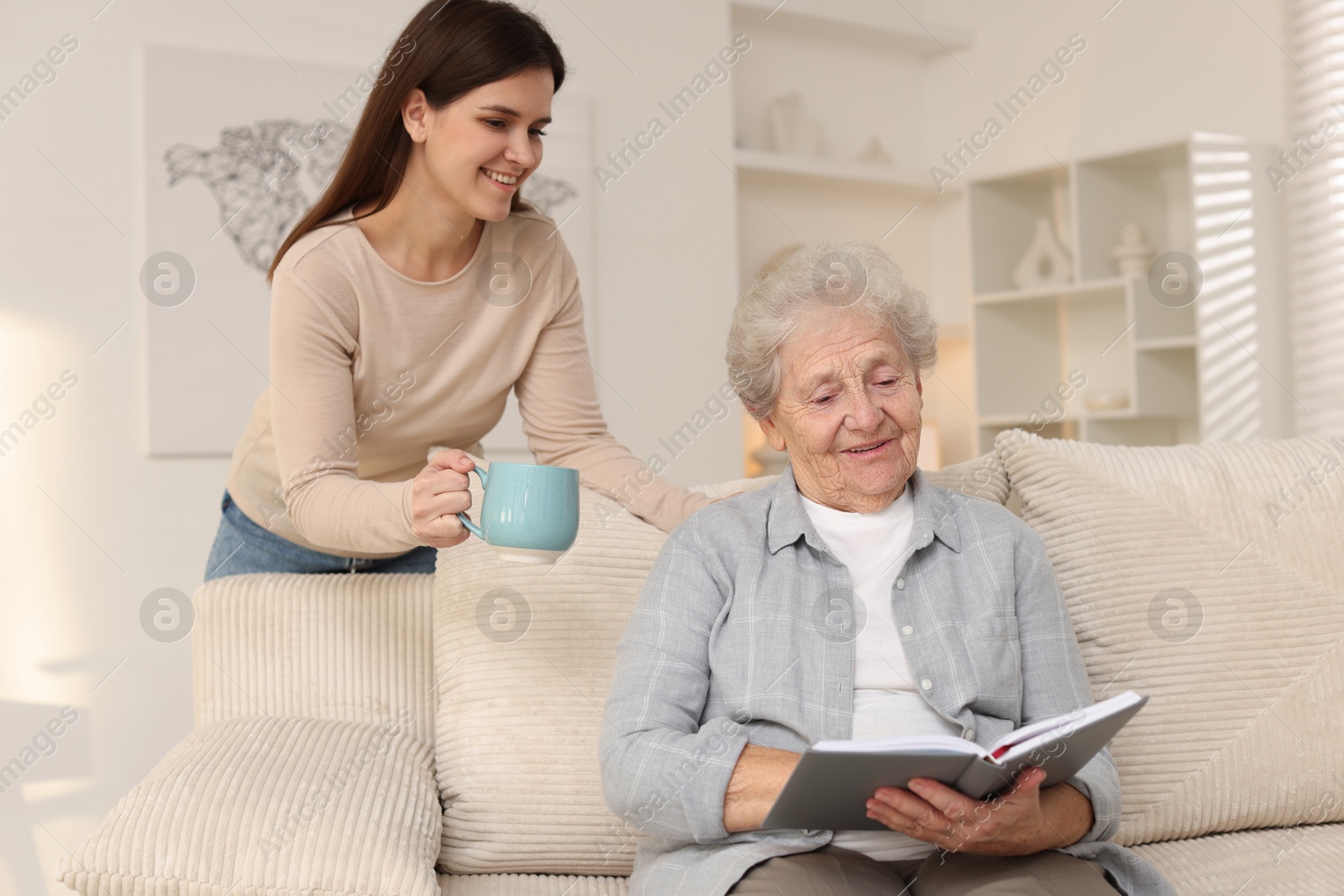 Photo of Granddaughter giving hot drink to her grandmother at home. Elderly care