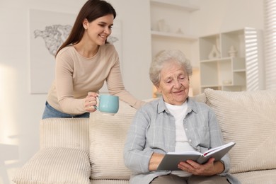 Photo of Granddaughter giving hot drink to her grandmother at home. Elderly care