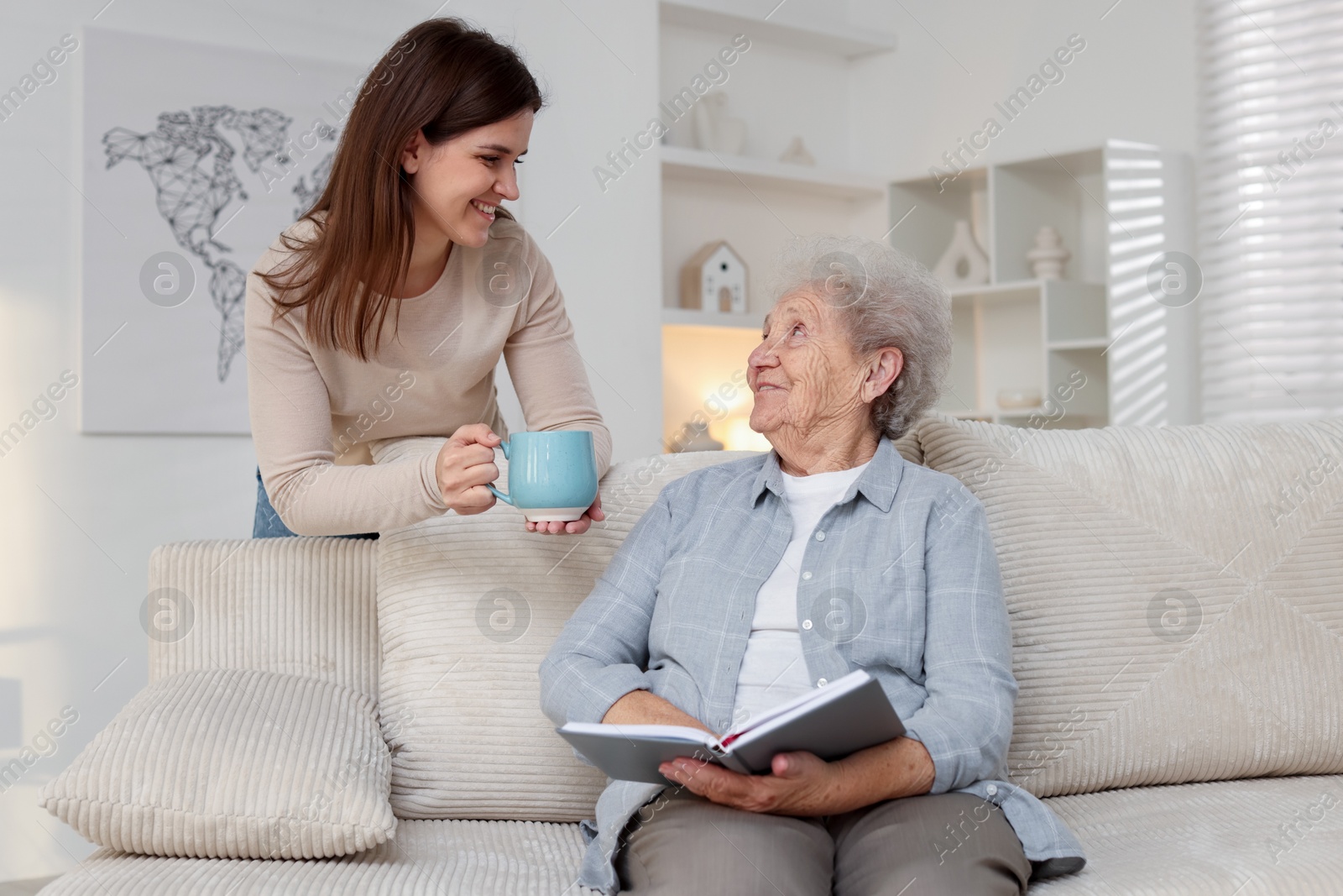 Photo of Granddaughter giving hot drink to her grandmother at home. Elderly care