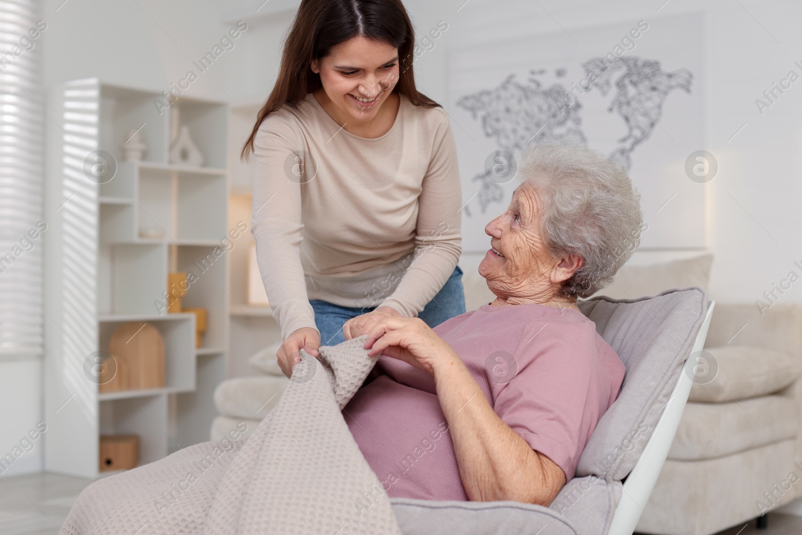 Photo of Granddaughter covering her grandmother with blanket at home. Elderly care