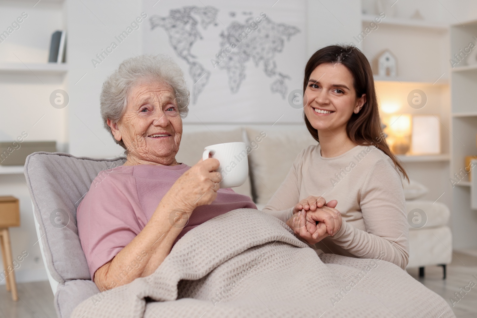 Photo of Grandmother with hot drink and her granddaughter at home. Elderly care