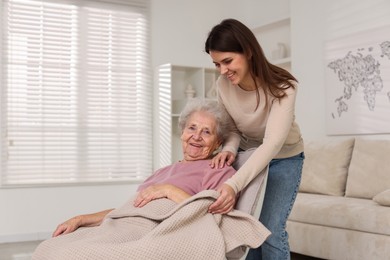 Photo of Granddaughter covering her grandmother with blanket at home. Elderly care