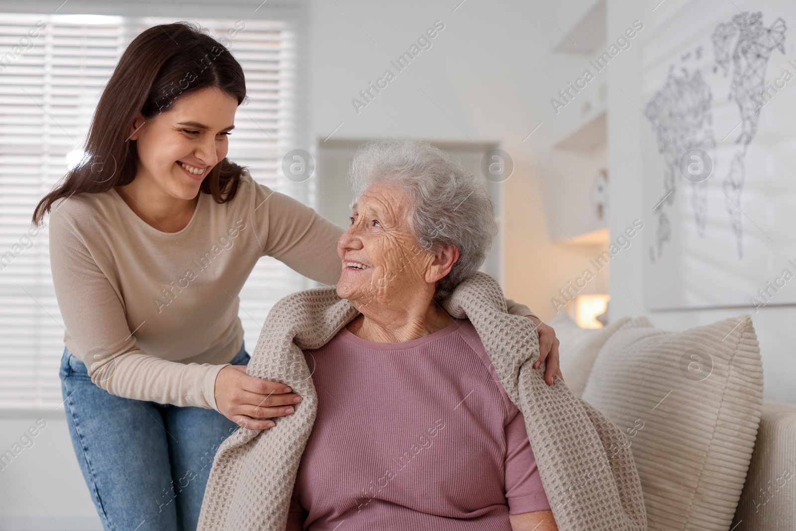 Photo of Granddaughter covering her grandmother with blanket at home. Elderly care