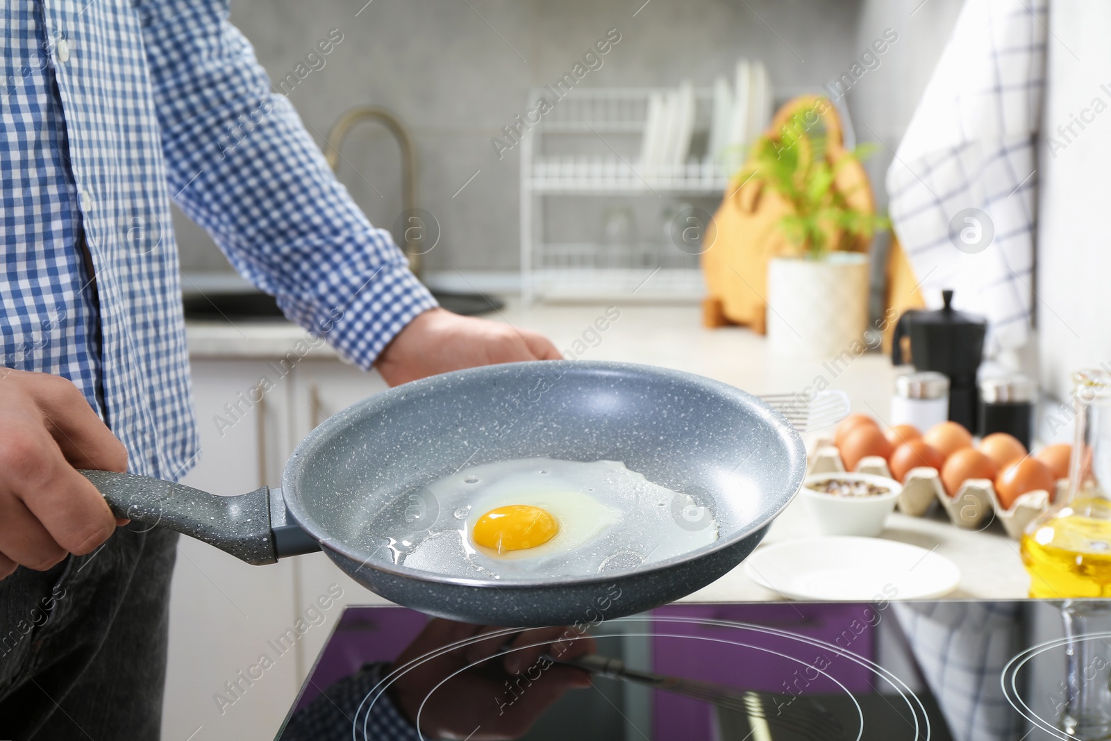 Photo of Man cooking egg in frying pan on cooktop indoors, closeup