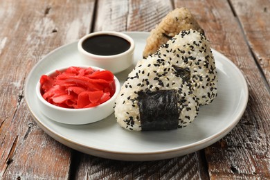 Photo of Rice balls (onigiri), soy sauce and pickled ginger on wooden table, closeup. Traditional Japanese dish