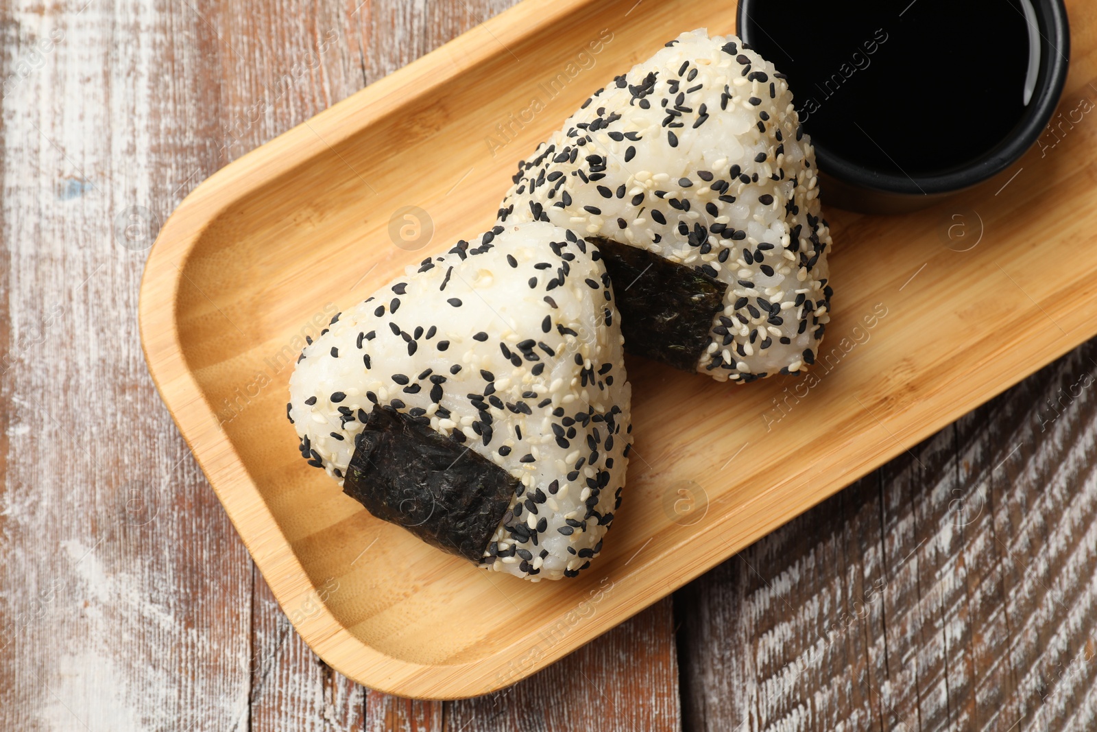 Photo of Rice balls (onigiri) and soy sauce on wooden table, top view. Traditional Japanese dish