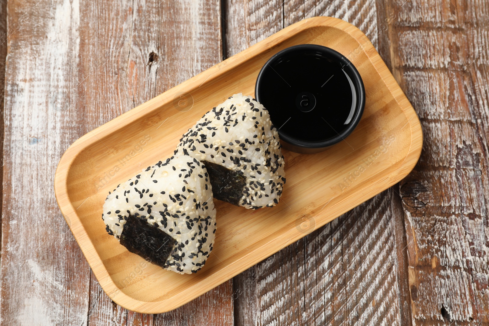 Photo of Rice balls (onigiri) and soy sauce on wooden table, top view. Traditional Japanese dish