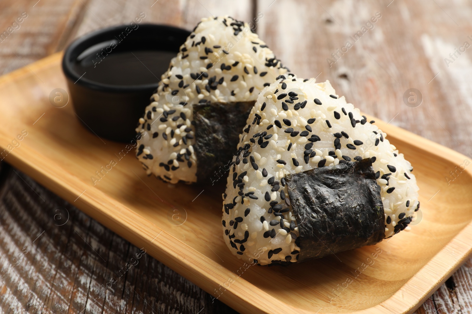 Photo of Rice balls (onigiri) and soy sauce on wooden table, closeup. Traditional Japanese dish