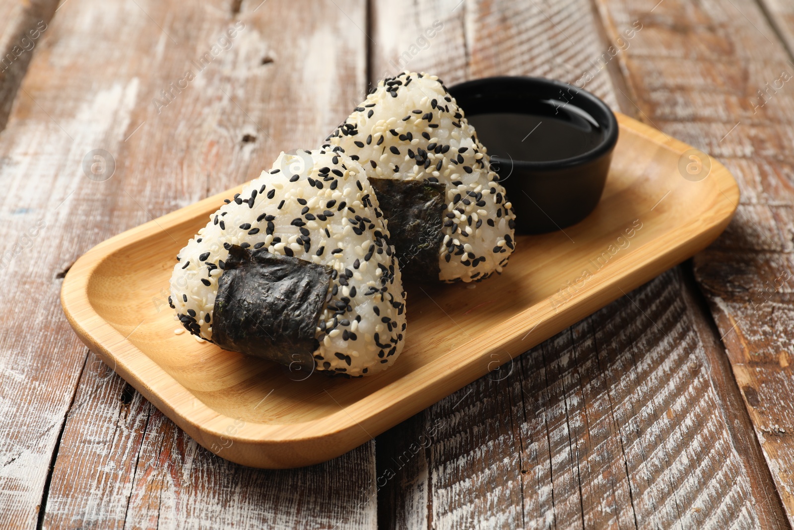 Photo of Rice balls (onigiri) and soy sauce on wooden table, closeup. Traditional Japanese dish