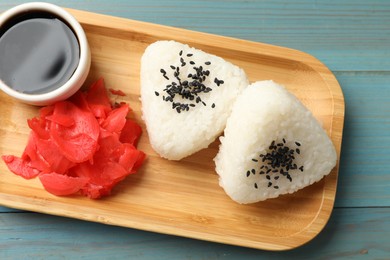 Photo of Rice balls (onigiri), soy sauce and pickled ginger on light blue wooden table, top view. Traditional Japanese dish