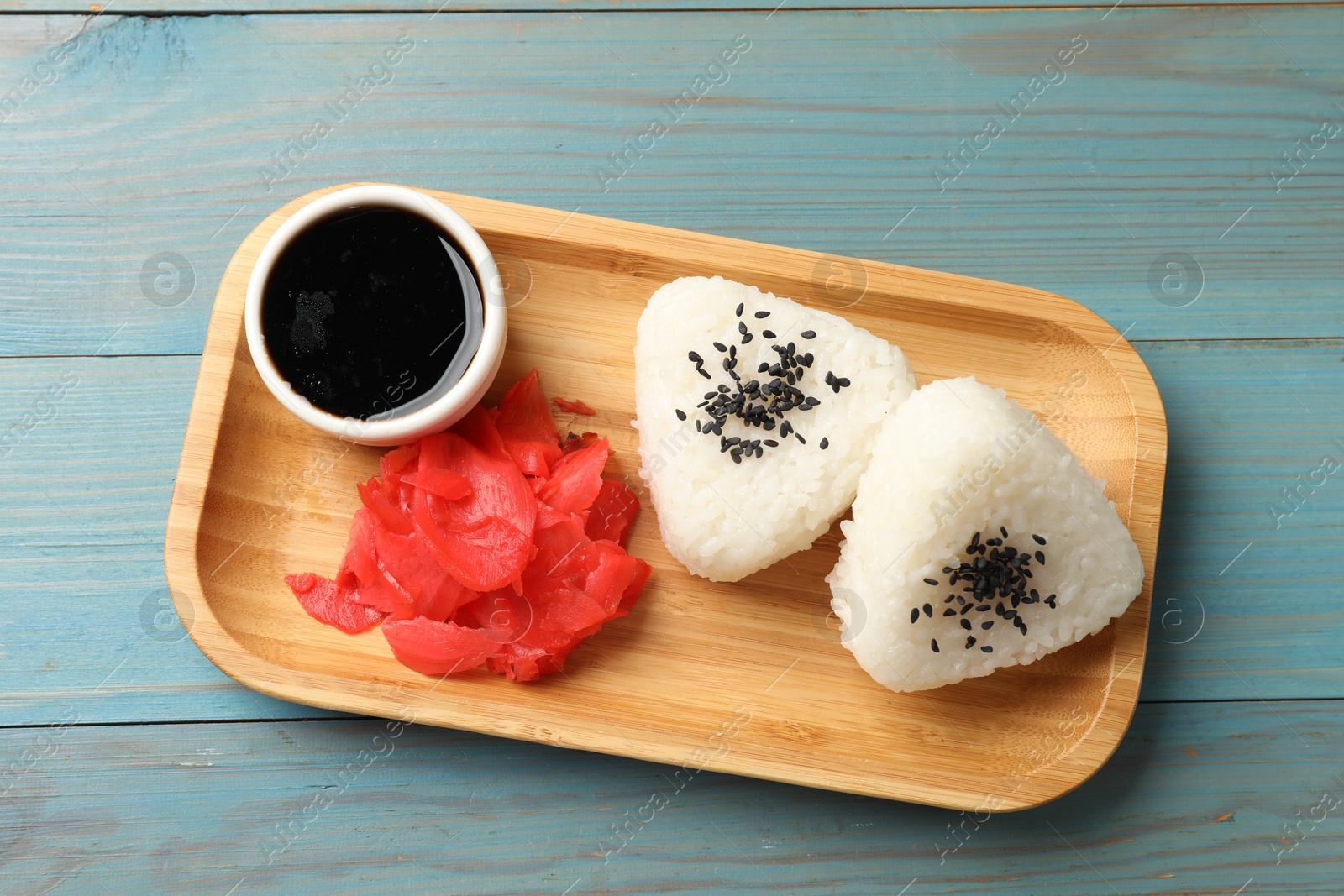 Photo of Rice balls (onigiri), soy sauce and pickled ginger on light blue wooden table, top view. Traditional Japanese dish