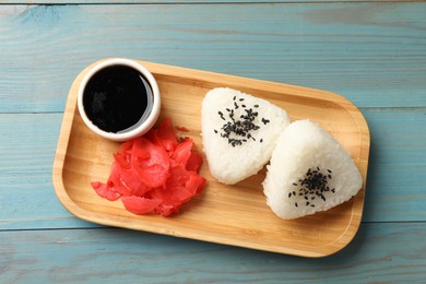 Photo of Rice balls (onigiri), soy sauce and pickled ginger on light blue wooden table, top view. Traditional Japanese dish