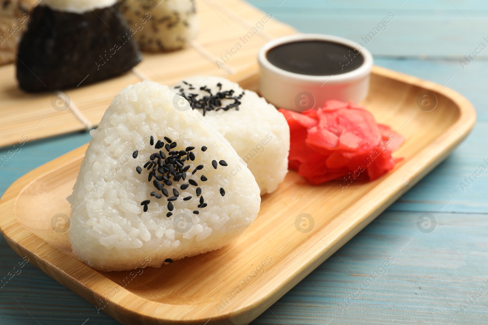 Photo of Rice balls (onigiri), soy sauce and pickled ginger on light blue wooden table, closeup. Traditional Japanese dish