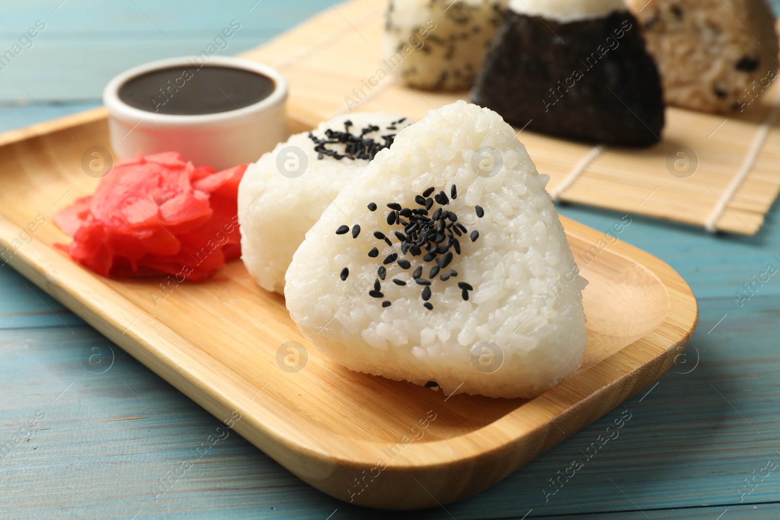 Photo of Rice balls (onigiri), soy sauce and pickled ginger on light blue wooden table, closeup. Traditional Japanese dish