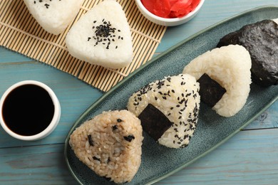 Photo of Rice balls (onigiri), soy sauce and pickled ginger on light blue wooden table, flat lay. Traditional Japanese dish