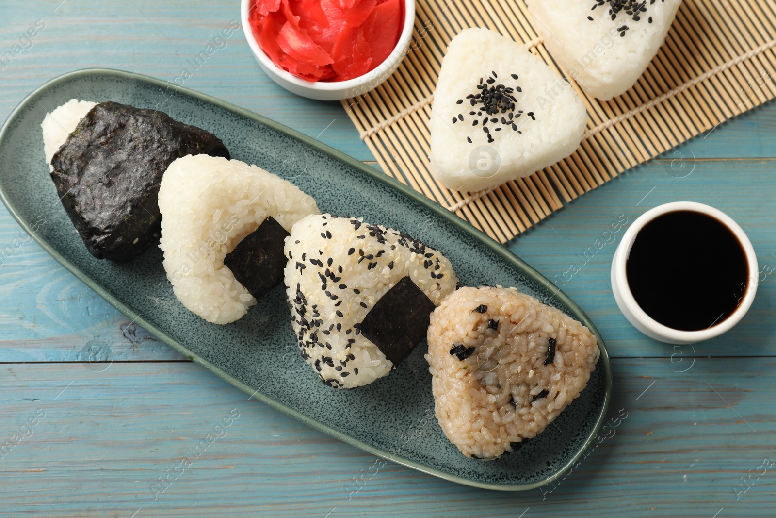 Photo of Rice balls (onigiri), soy sauce and pickled ginger on light blue wooden table, flat lay. Traditional Japanese dish