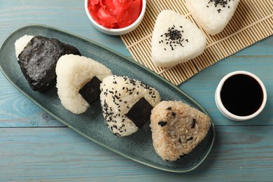 Photo of Rice balls (onigiri), soy sauce and pickled ginger on light blue wooden table, flat lay. Traditional Japanese dish