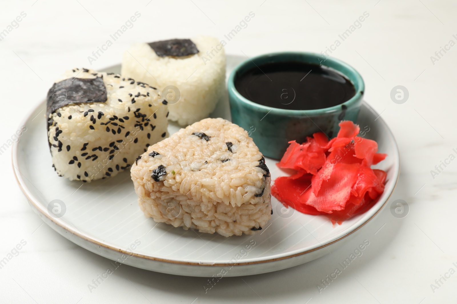 Photo of Rice balls (onigiri), soy sauce and pickled ginger on light table, closeup. Traditional Japanese dish