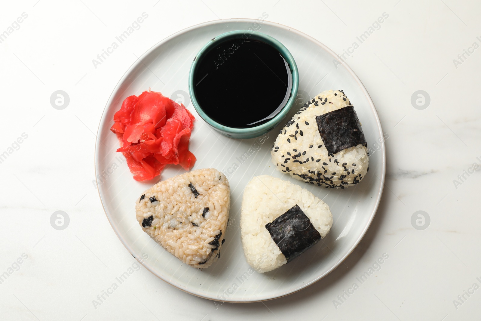 Photo of Rice balls (onigiri), soy sauce and pickled ginger on light table, top view. Traditional Japanese dish