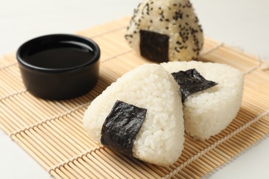 Photo of Rice balls (onigiri) and soy sauce on light table, closeup. Traditional Japanese dish