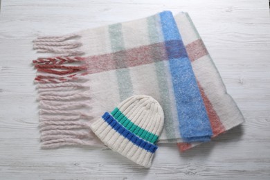 Photo of Soft scarf and knitted hat on wooden table, top view