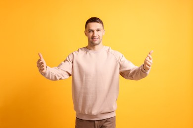 Photo of Cheerful man welcoming guests on orange background