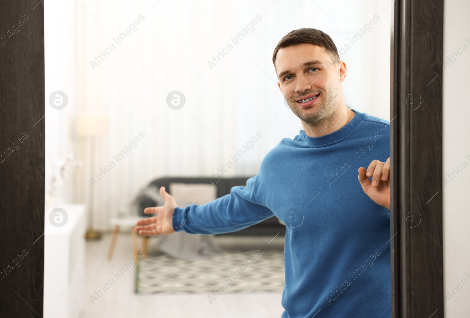 Photo of Cheerful man welcoming guests to his apartment. Space for text