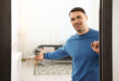 Photo of Cheerful man welcoming guests to his apartment. Space for text