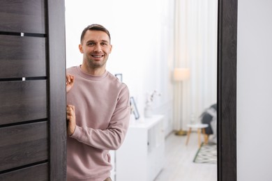 Cheerful man welcoming guests to his apartment. Space for text