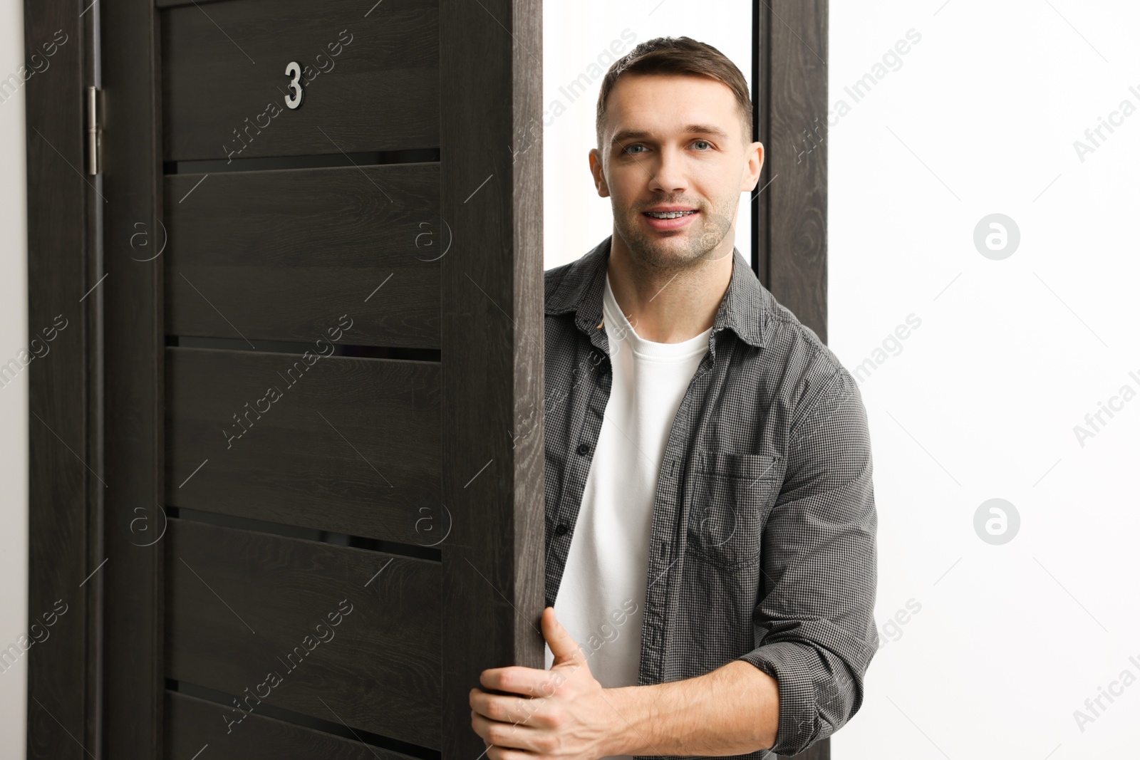 Photo of Cheerful man meeting guests in doorway of his apartment