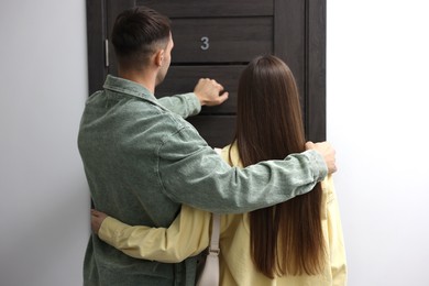 Photo of Couple knocking on door of their neighbors apartment, back view