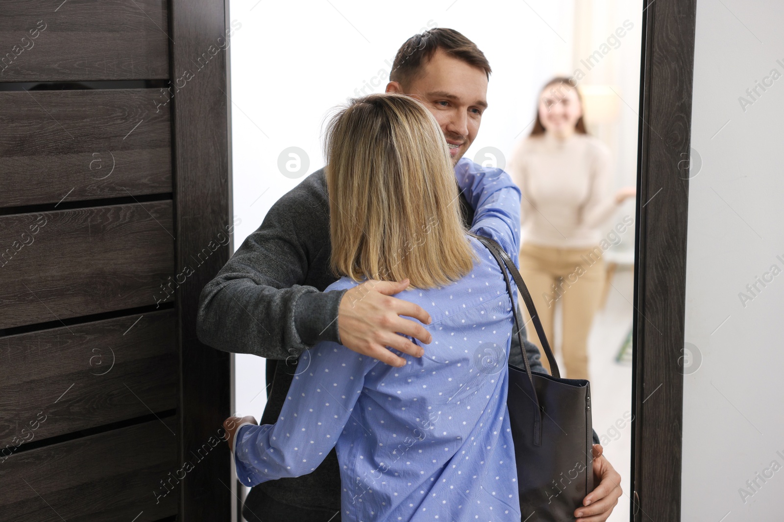 Photo of Lovely couple welcoming friend to their apartment, selective focus