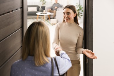 Photo of Happy woman greeting neighbor and welcoming her to apartment