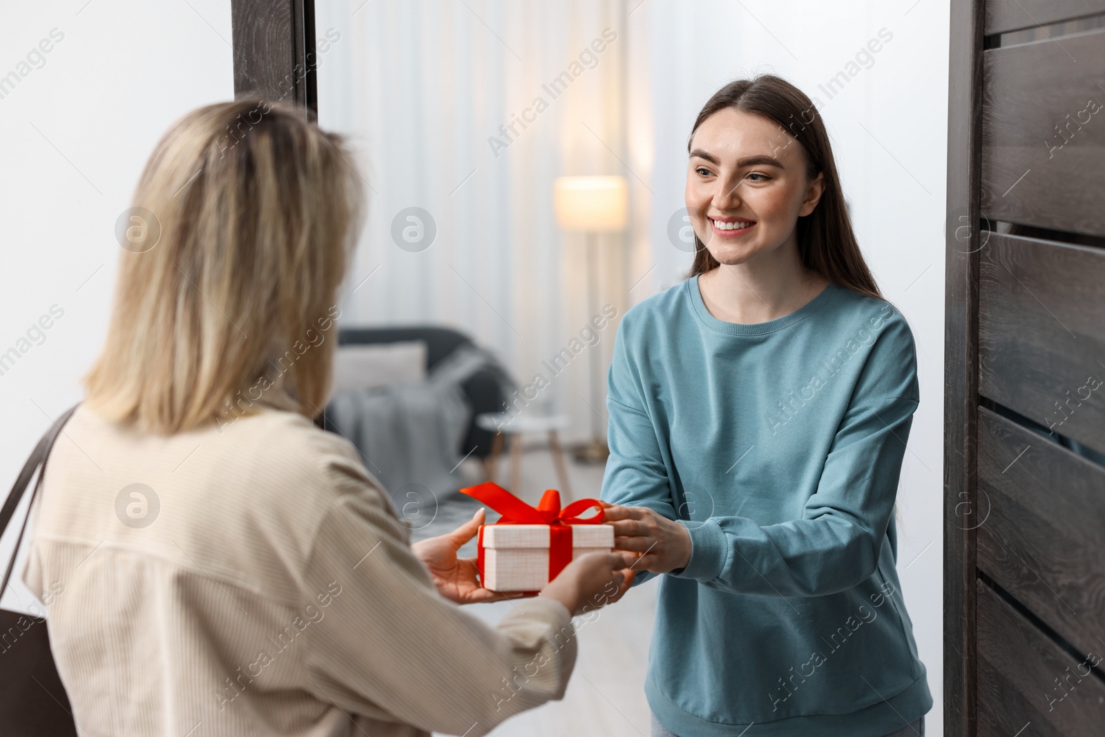 Photo of Woman giving housewarming gift to her friend at new apartment