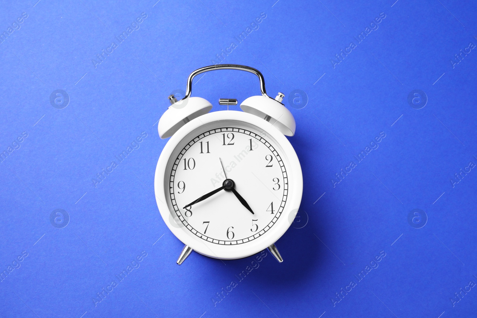One white alarm clock on blue background, top view Photo of One white alarm clock on blue background, top view
