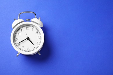 Photo of One white alarm clock on blue background, top view. Space for text