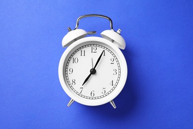 Photo of One white alarm clock on blue background, top view