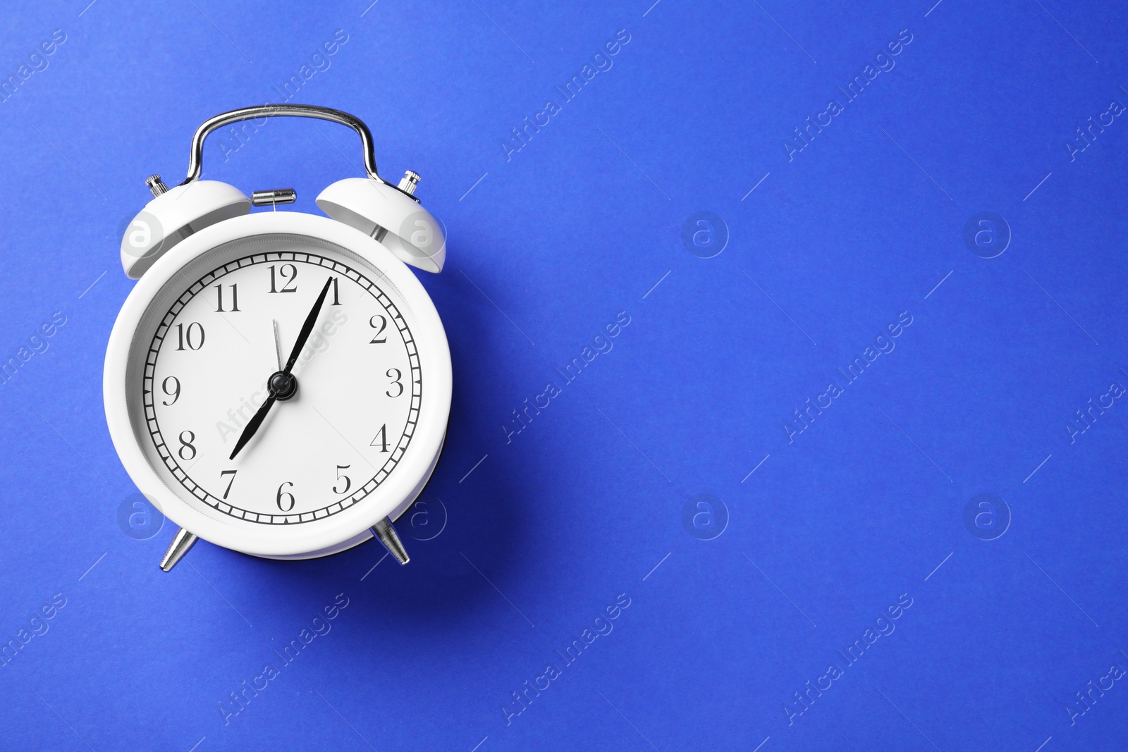 One white alarm clock on blue background, top view. Space for text Photo of One white alarm clock on blue background, top view. Space for text
