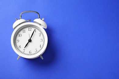 Photo of One white alarm clock on blue background, top view. Space for text