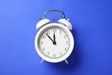 Photo of One white alarm clock on blue background, top view