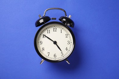 Photo of One black alarm clock on blue background, top view