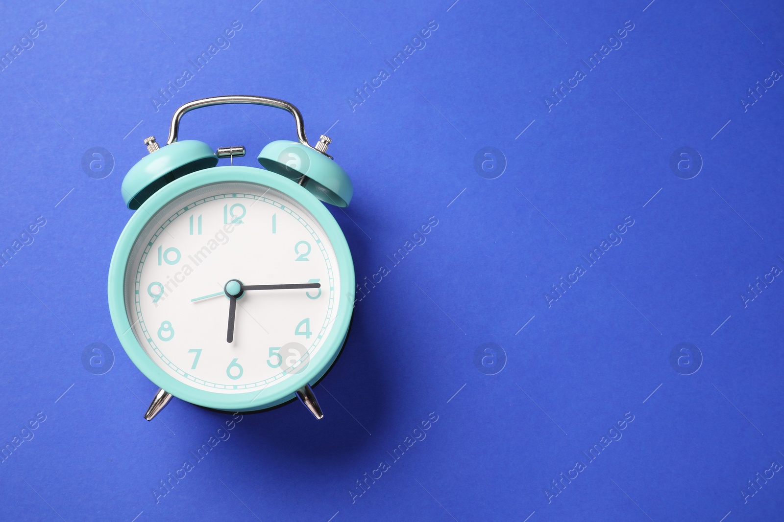One turquoise alarm clock on blue background, top view. Space for text Photo of One turquoise alarm clock on blue background, top view. Space for text