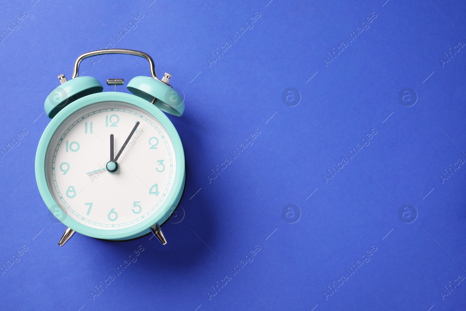 One turquoise alarm clock on blue background, top view. Space for text Photo of One turquoise alarm clock on blue background, top view. Space for text