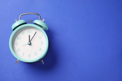 Photo of One turquoise alarm clock on blue background, top view. Space for text