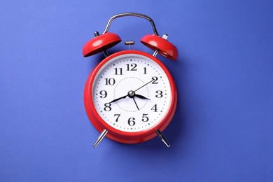 Photo of One red alarm clock on blue background, top view