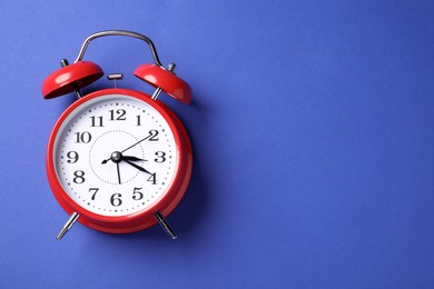 Photo of One red alarm clock on blue background, top view. Space for text