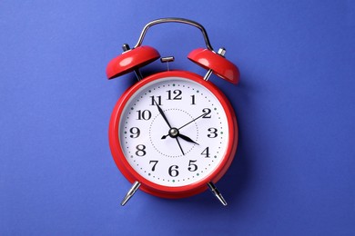 Photo of One red alarm clock on blue background, top view