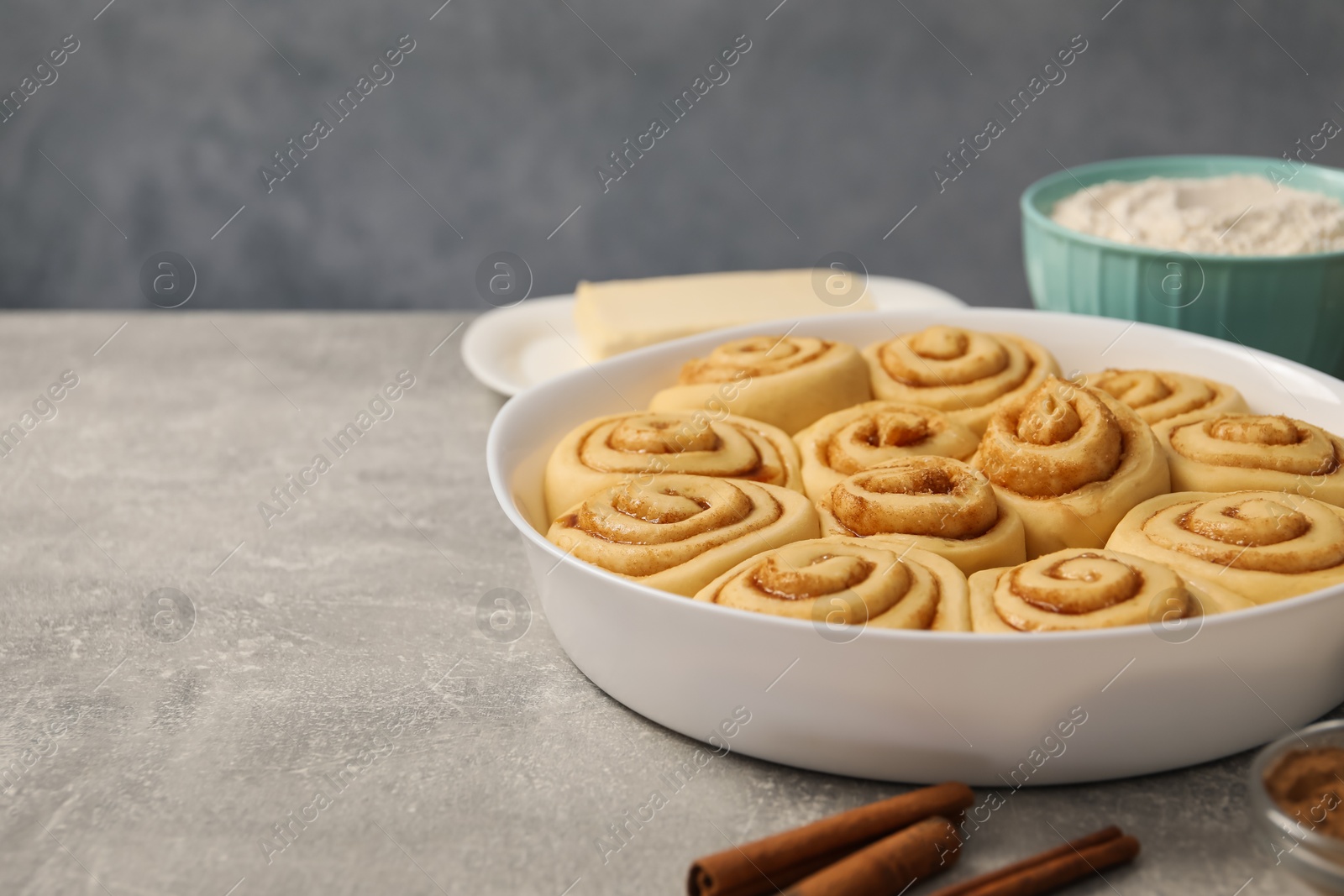 Photo of Raw cinnamon rolls in baking dish on light grey table, closeup. Space for text