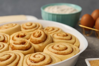 Photo of Raw cinnamon rolls in baking dish on table, closeup