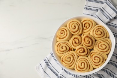 Raw cinnamon rolls in baking dish on white marble table, top view. Space for text